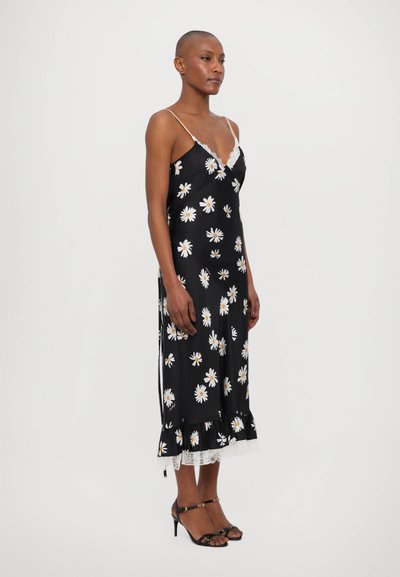 Robe noire en satin avec imprimé marguerite blanche, dentelle en finition, et bretelles ajustables. Elle possède un ourlet volé et une fente sur le côté pour un détail supplémentaire.