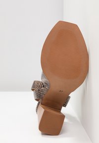 Klackskor med ett texturerat mönster av ormskinn i grå och beige nyanser, med rundad tå och en stabil blockklack. Storlek 37 synlig.