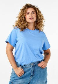 Maglietta di cotone blu chiaro con maniche corte e scollo rotondo, abbinata a pantaloni corti in denim blu a vita alta. Design minimalista, texture liscia.