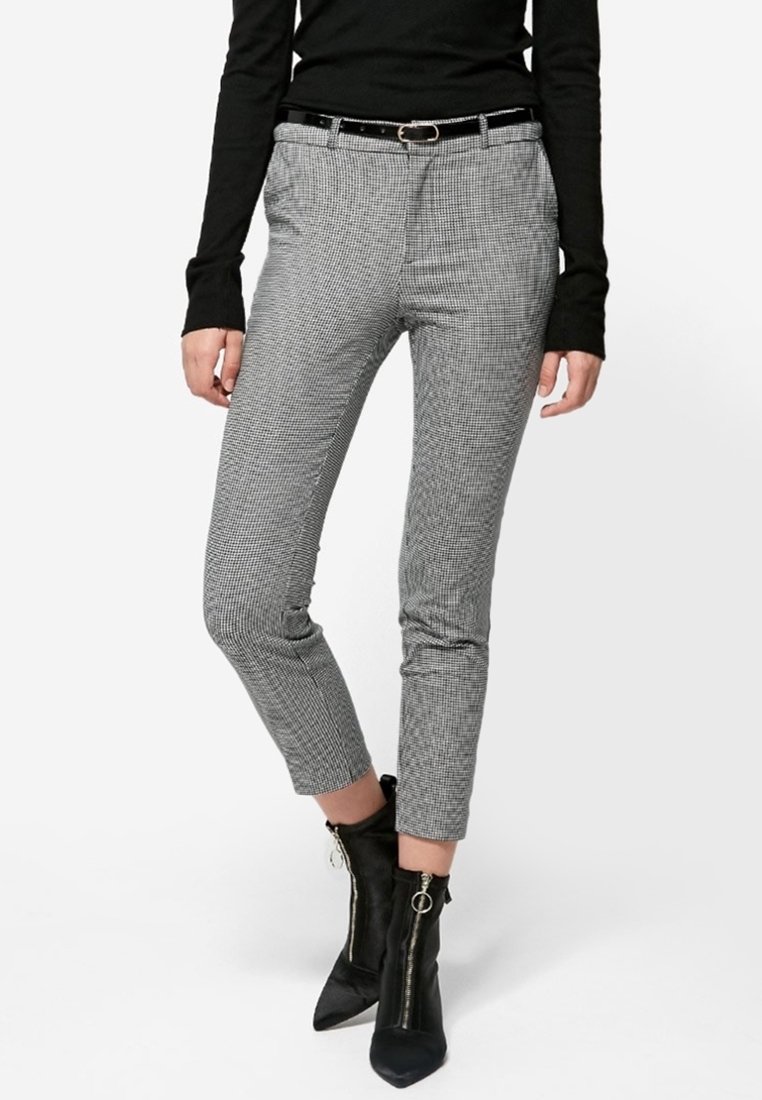 Femme portant un haut noir à manches longues, un pantalon slim gris à motif pied-de-poule avec ceinture noire, et des bottines noires à fermeture éclair.