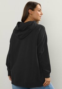 Felpa nera con cappuccio realizzata in tessuto morbido, presenta un cappuccio regolabile, maniche lunghe e una vestibilità comoda. Mostra un design minimalista con polsini a coste.