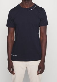 Tmavě modré bavlněné tričko s krátkými rukávy a kulatým výstřihem, s bílým logem "TOMMY HILFIGER" u ramene a nápisem "NEW YORK, EST. 1985" na lemu.