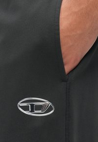 Μαύρα αθλητικά σορτς από υφασμάτινη υφή, με ασημί λογότυπο στο πλάι και λεπτομέρεια με πλαϊνή τσέπη.