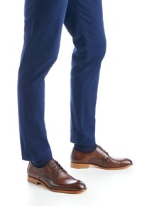 Braune Lederschuhe mit glattem Finish, Schnürsenkeln und einer hellen Gummisohle, kombiniert mit marineblauen Hosen.