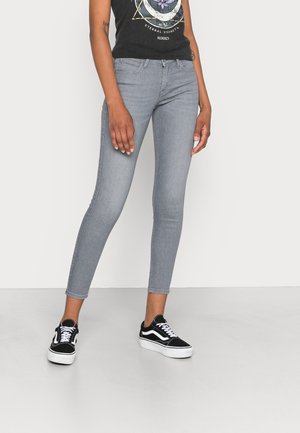 Jeans ajustados grises con una textura suave, cintura alta y pierna ceñida. Combinados con zapatillas de deporte en blanco y negro. Un atuendo simple y casual.