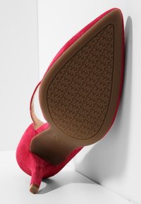 Scarpa con tacco alto in suede rosso vista dal retro, con punta appuntita e suola marrone testurizzata con dettagli di branding.