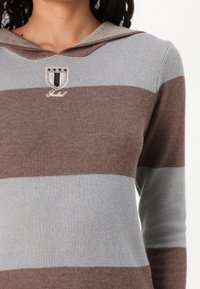 Felpa con cappuccio a righe orizzontali marroni e grigio chiaro, realizzata in tessuto morbido. Presenta uno stemma ricamato e il logo sul petto.