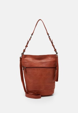Bruine leren bucketbag met verstelbare schouderriem, voorvak met rits en kwastdetail, afgebeeld tegen een effen achtergrond.