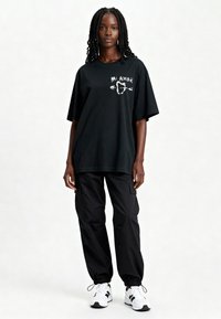T-shirt oversize noir avec un graphic blanc "Mi Amor" et des flèches, associé à un pantalon cargo noir et des baskets blanches avec des accents noirs.