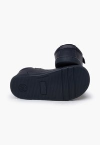 Calzado negro con una suela de goma texturizada, material superior liso y una correa segura. Presenta un branding mínimo en la suela.