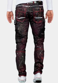 Zwarte en bordeaux rode jeans met spetterpatronen, textuurstof, cargozakken en zilveren accenten, gecombineerd met witte sneakers.