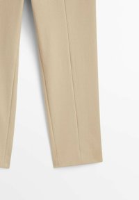 Pantalon beige confectionné sur mesure avec des jambes droites et un pli vertical visible au centre de chaque jambe.