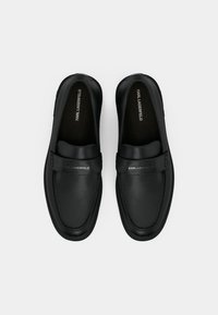 Μαύρα δερμάτινα παπούτσια slip-on με στρογγυλεμένες μύτες, με κεντρικό λουράκι και ανάγλυφο λογότυπο. Λείο υλικό με ελάχιστες ραφές.