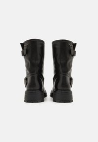 Botas de couro pretas até ao meio da panturrilha, com bico arredondado, dois fechos de fivela laterais e uma sola grossa e texturizada. Acabamento suave com ligeiro brilho.