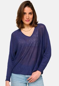 Pull en maille léger bleu marine avec un décolleté en V et des manches longues, présentant une coupe décontractée et une subtile transparence dans le tissu.