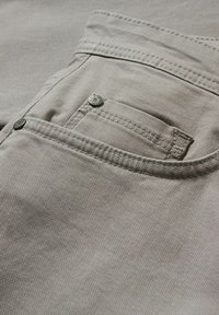Gros plan sur un tissu en denim beige montrant une poche avant avec des rivets métalliques et des détails de couture visibles.