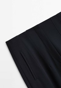 Pantalon noir sur mesure avec un détail de poche verticale fine sur le côté, présenté sur fond blanc.
