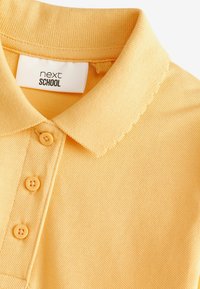 Gul polo t-shirt med en texturerad tyg, en klassisk krage, tre matchande knappar och en etikett som läser "next SCHOOL."