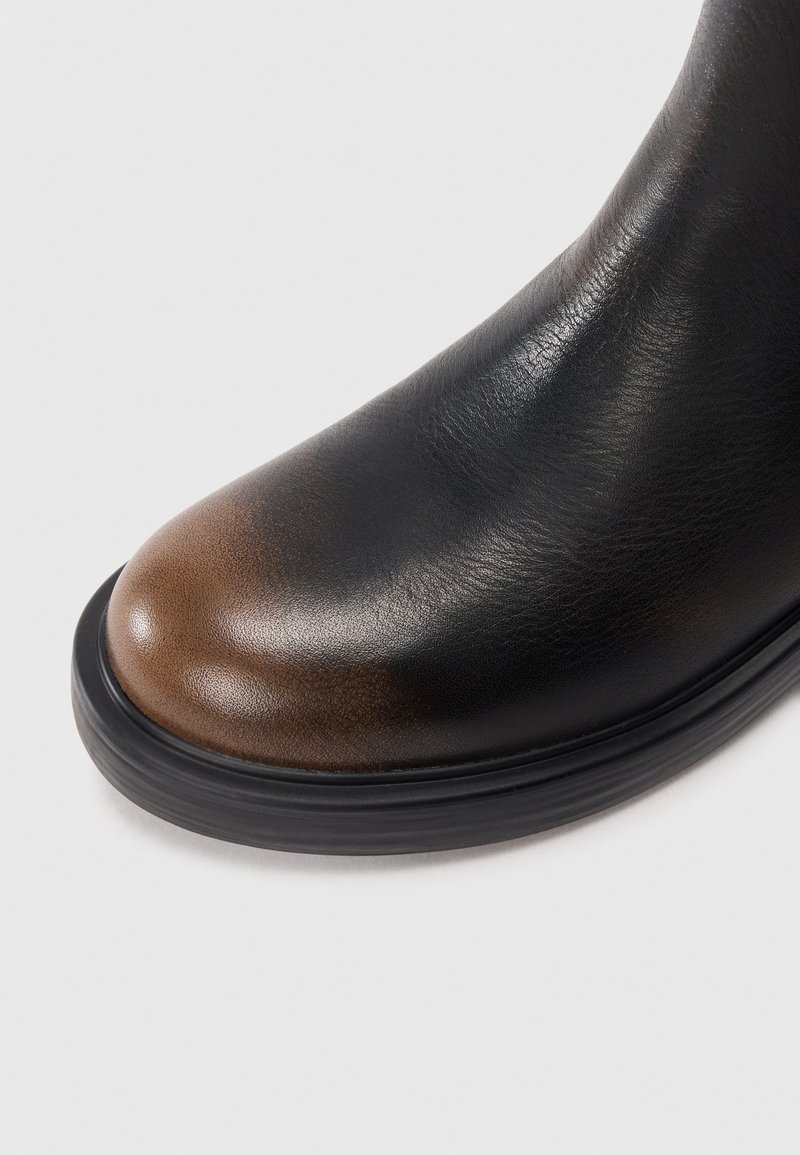 Black leather boot with a rounded toe featuring a brown gradient, and a thick black sole on a white background.