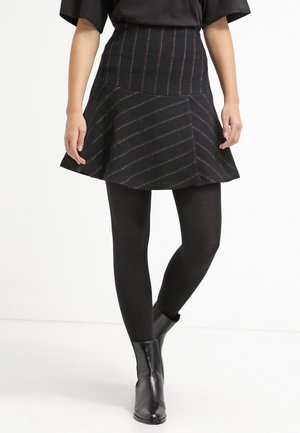 Jupe noire évasée avec des rayures diagonales dans des couleurs contrastées, assortie à des leggings noirs et des bottines. Texture lisse et taille ajustée.