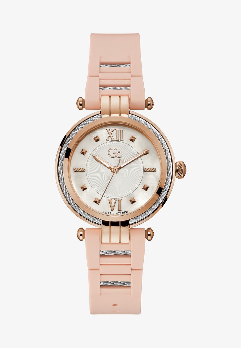 Ümmargune kell roosi kullast korpusega, valge pärlmutterist kellapaneel, roosa silikoonist rihm ja hõbedased detailid. Märgid 12. ja 6. kohal.