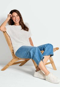 Lichtgewicht, textuurgebreide witte trui met korte mouwen, gecombineerd met blauwe denim culottes en witte sneakers, zittend op een houten stoel.