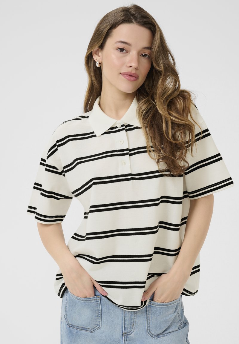 Polo rayé en blanc cassé avec des rayures noires, manches courtes, col classique et patte de boutonnage. Matière douce, coupe décontractée.