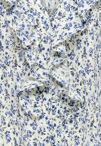 Tissu blanc avec petit imprimé floral bleu, présentant une bordure froncée verticale au centre.