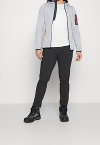 Szara polarowa kurtka z granatowymi akcentami, z pełnym zamkiem błyskawicznym i boczną kieszenią; zestawiona z czarnymi spodniami i solidnymi czarnymi butami trekkingowymi.