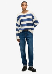 Suéter de rayas gruesas en crema y azul, con un ajuste relajado. Combinado con jeans azules de pierna recta y botas negras con cordones.