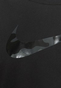 Camiseta negra con un logo Swoosh de Nike en camuflaje brillante. La tela parece suave, con un cuello redondo y mangas cortas.