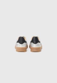Sølv sneakers med svart hælhette og beige detaljer, med en teksturert gummisåle. Designet er minimalistisk og moderne.