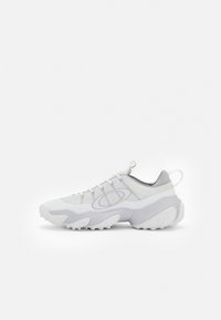 Weiße Sportschuhe mit einem Mesh-Obermaterial, abgerundeter Zehenpartie und einer strukturierten Gummisohle mit ausgeprägten Traktionsnoppen. Helle graue Akzente überall.