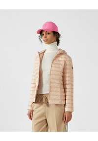 Giacca puffer rosa chiaro con zip frontale e cappuccio, indossata sopra un dolcevita bianco a coste. Abbinata a pantaloni beige con lacci. Berretto rosa.