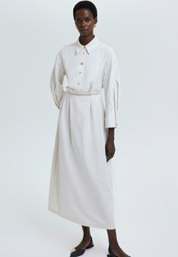 Biele ľanové šaty s golierom, zapínaním na gombíky vpredu, opaskom v páse a objemnými rukávmi; hladký, elegantný dizajn.