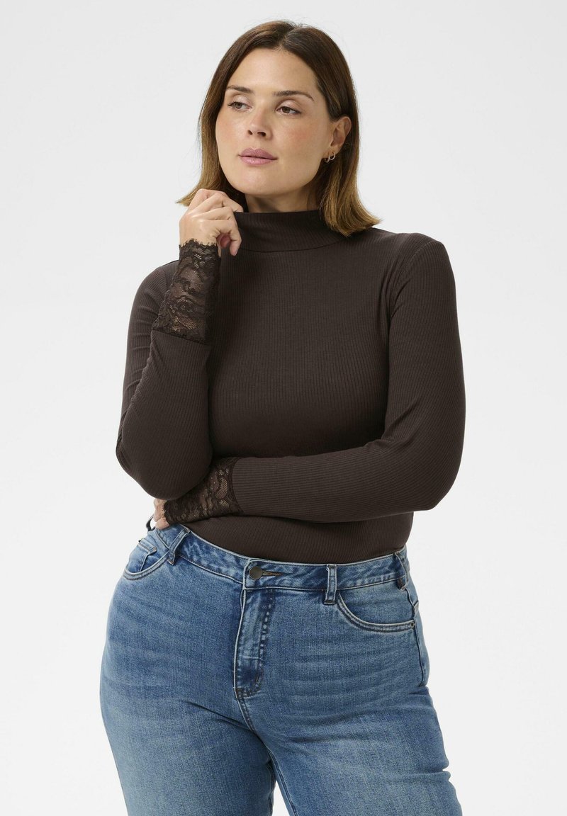 Brun ribbad polokrage med spetsdetaljer vid handledarna, parat med ljusblå högmidjade jeans. Enkel vit bakgrund.