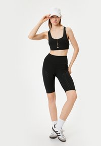 Svart atletisk crop top med knapprad framtill, ihop med höga svarta cykelbyxor med perforerade mönster och en slät textur.