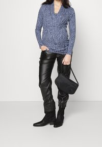 Námořnická halenka s dlouhým rukávem a vzorovanou texturou, spárovaná s lesklými černými umělými koženými kalhotami a malou černou kabelkou s řetízkovým popruhem.