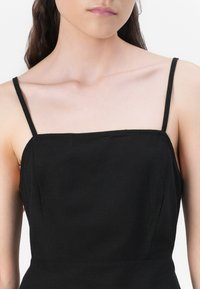 Robe noire sans manches avec des bretelles fines, un décolleté carré et une texture lisse, mettant en valeur un design minimaliste et des lignes épurées.