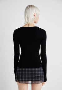 Svart langermet topp med en tettsittende design, sammen med et kort rutete skjørt med en gjennomsiktig kant og grønt og hvitt rutemønster.