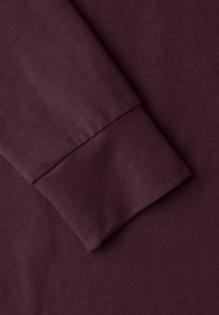 Langärmliges Kleidungsstück aus tiefbordeauxfarbenem Stoff; glatte Textur mit einem enganliegenden Bündchen. Weiches, elastisches Strickmaterial.