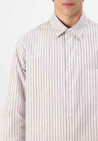 Chemise à manches longues à boutons de couleur rose clair avec de fines rayures verticales vertes et blanches. Présente un col pointu et une poche poitrine.