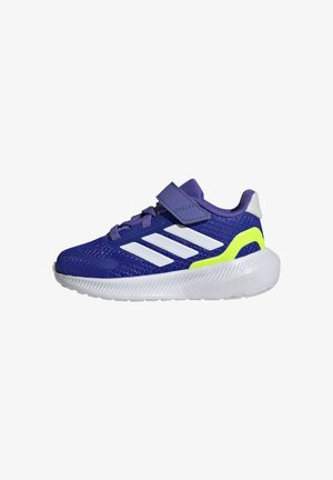 Zapatilla deportiva morada con franjas blancas y acentos amarillos. Presenta un upper de tejido texturizado, un collar acolchado y una correa de velcro.