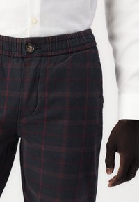 Marineblauwe geblokte broek met een zachte textuur, voorzien van een relaxte tailleband, knoopsluiting en contrasterende rode lijnen in het ruitpatroon.