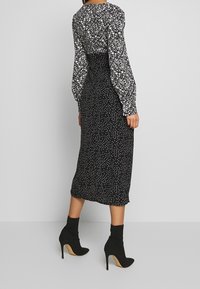 Vestido negro con lunares blancos, mangas largas abullonadas y cintura ceñida, combinado con botas de tacón altas hasta el tobillo en negro.