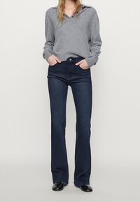 Gray long-sleeve polo shirt with a button-down collar, paired with dark blue flared jeans. Both garments feature a smooth texture.