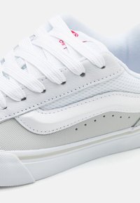 Weißer Sneaker mit einem Obermaterial aus Mesh und Leder, mit strukturierten Akzenten, flachen Schnürsenkeln und einer Gummisohle. Auffälliges seitliches Design und Belüftungsöffnungen.