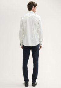 White long-sleeve shirt with button cuffs, paired with navy trousers. Features a subtle textured pattern and a slightly fitted design.