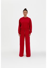 Roter Sweatshirt und weit geschnittene Hose aus weichem Stoff, mit lockerer Passform und seitlichen Reißverschlüssen an der Hose für zusätzlichen Detail.