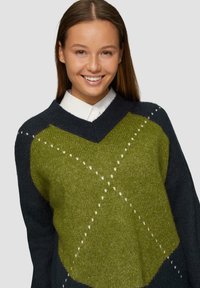Sweter dzianinowy z dekoltem w kształcie litery V, w ciemnogranatowej bazie z dużym zielonym wzorem w romby i białymi akcentami z przeszycia. Miękka faktura.